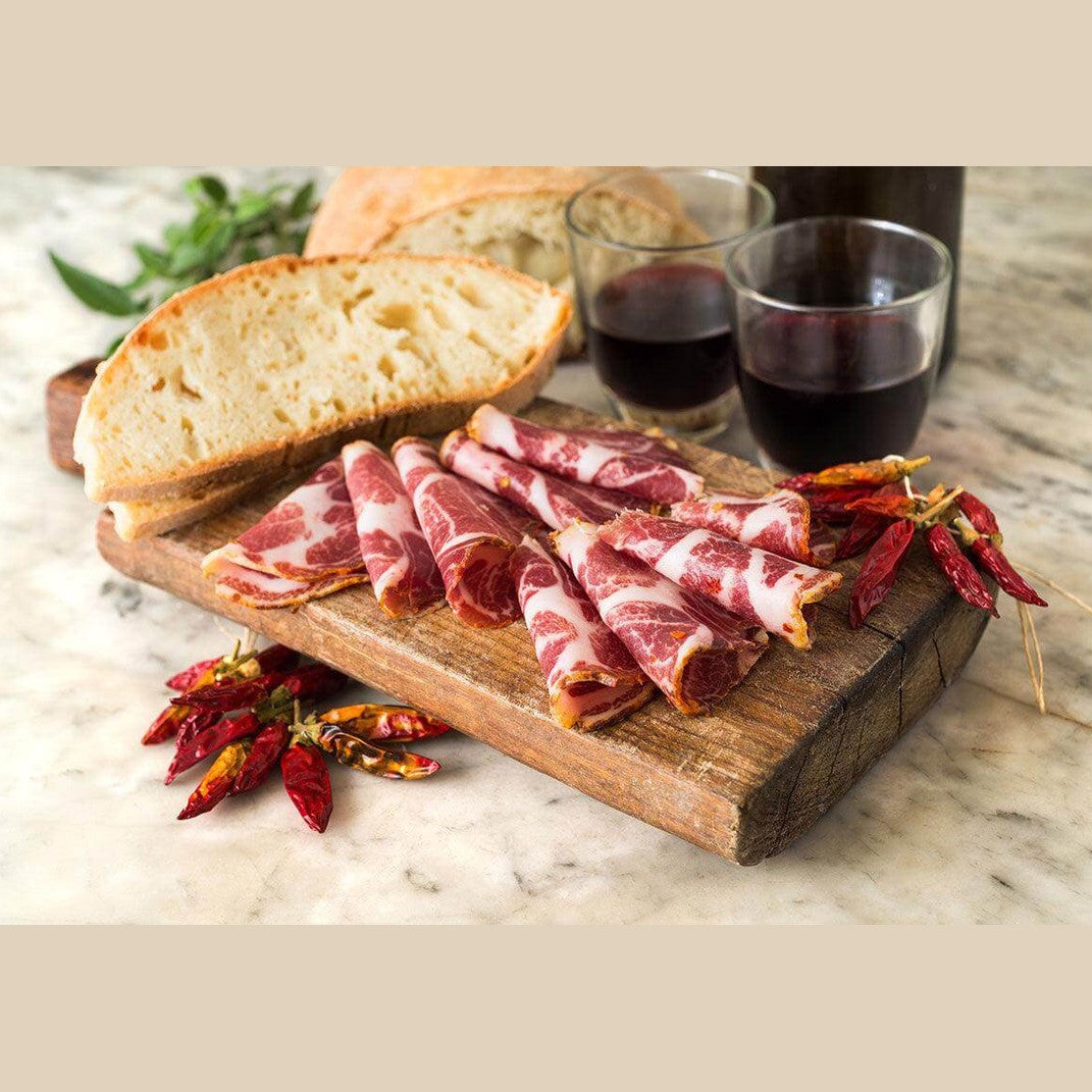 Delicious Capocollo legato a mano with bread, red wine, and chilies, showcasing Calabria's prized salumi.