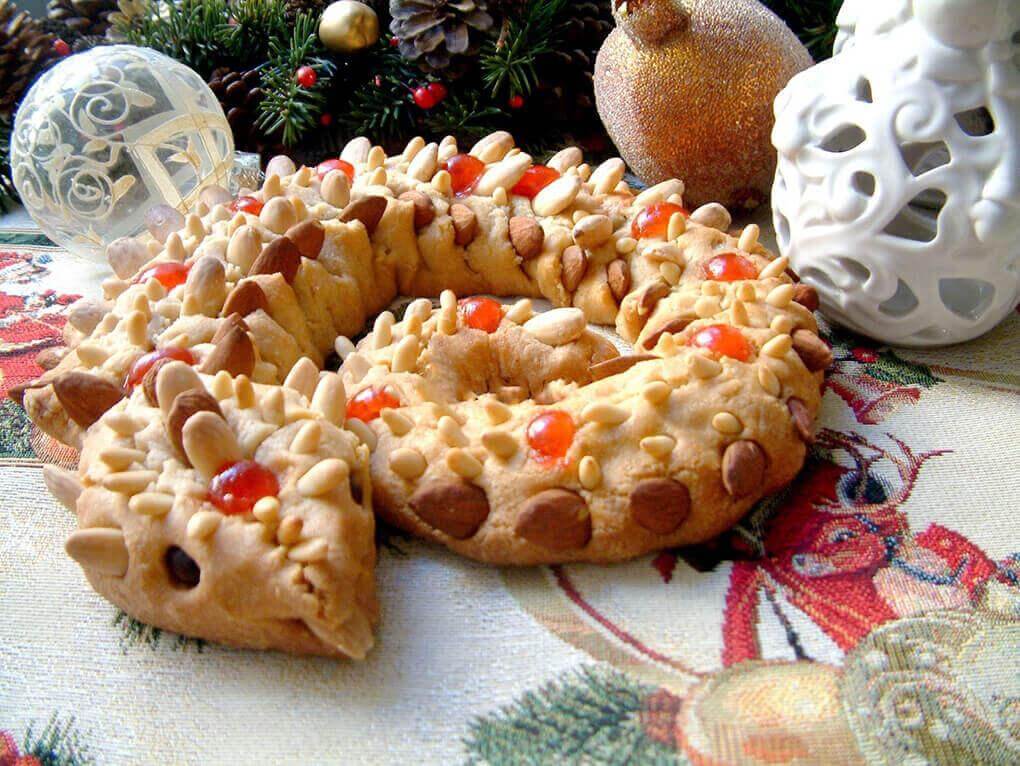 Decorative almond cookie shaped like a serpent, adorned with nuts and colorful candied fruits, festive table setting.