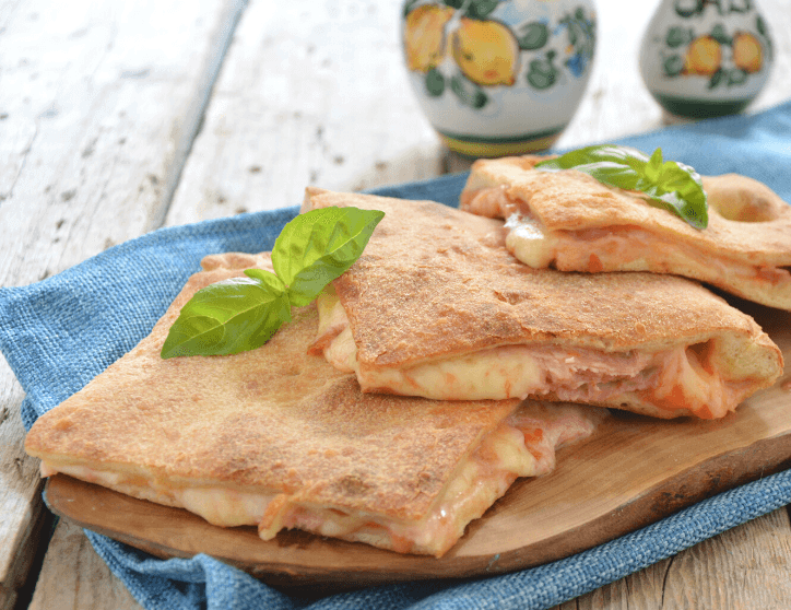 Pizza coperta calabrese con acciughe, olive, capperi e provola tagliata a metà su tagliere
