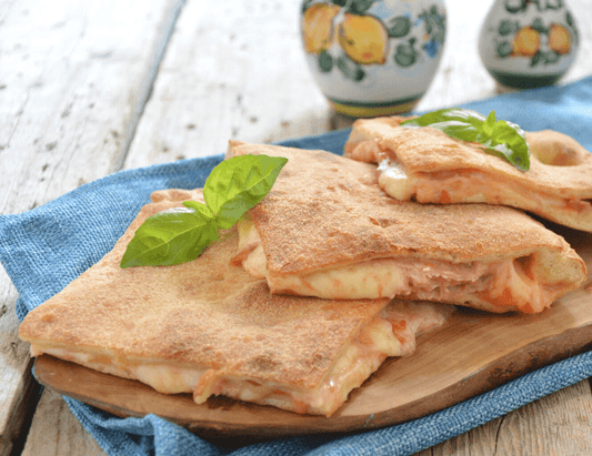 Pizza coperta calabrese con acciughe, olive, capperi e provola tagliata a metà su tagliere