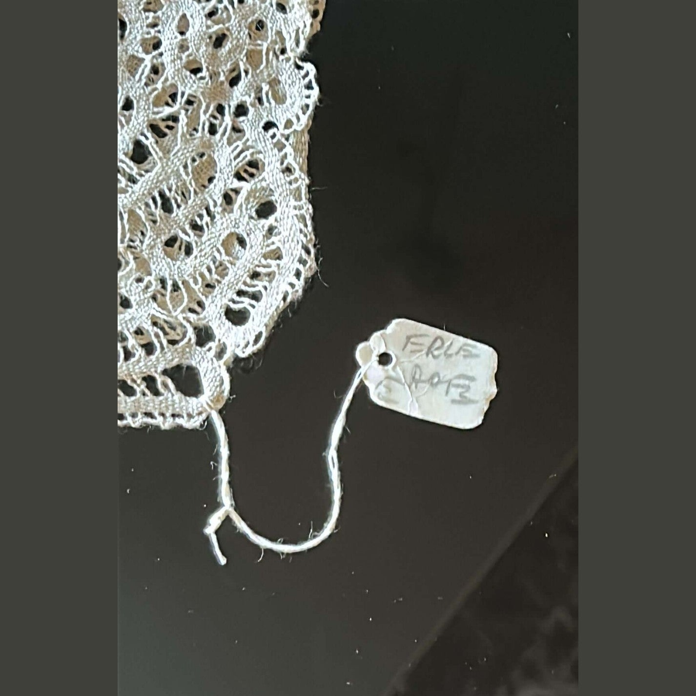 Close-up of intricate Burano lace with a tag reading 'FRL 248' on a dark surface.