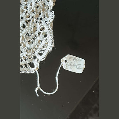 Close-up of intricate Burano lace with a tag reading 'FRL 248' on a dark surface.