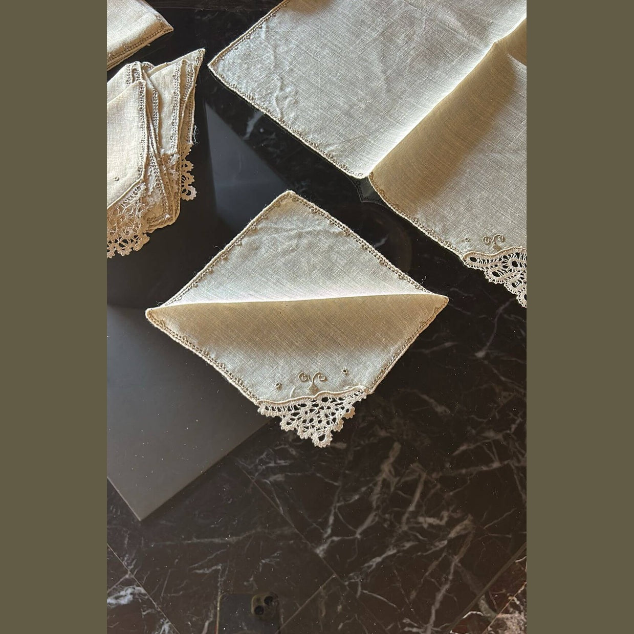 Set of vintage Burano lace napkins displayed on a dark marble table, showcasing intricate craftsmanship.