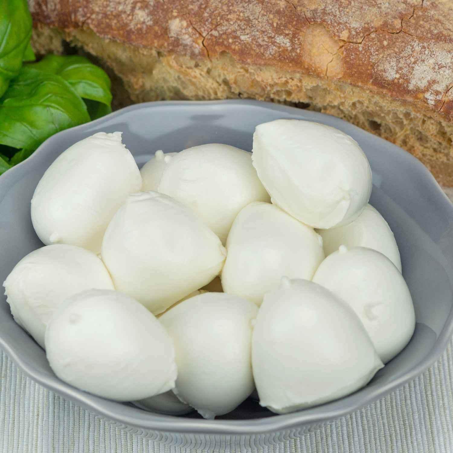 Bocconcini mozzarella bufala campana fresh dairy cheese in bowl with bread and basil leaves.