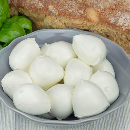 Bocconcini mozzarella bufala campana fresh dairy cheese in bowl with bread and basil leaves.