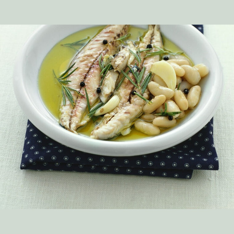 Filetti Sgombro al bergamotto su un letto di fagioli bianchi, con rosmarino e pepe in un piatto bianco.