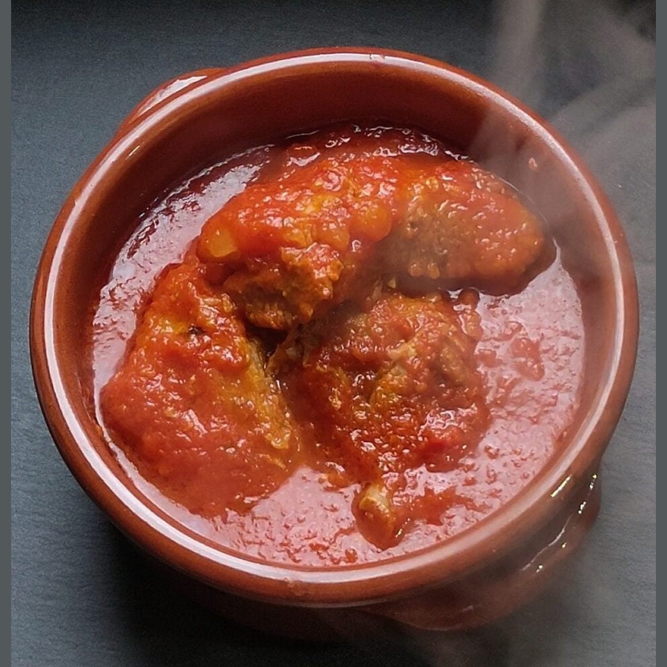 Ragù di maiale pronto alla calabrese in un contenitore di terracotta fumante, ricco di sugo di pomodoro.