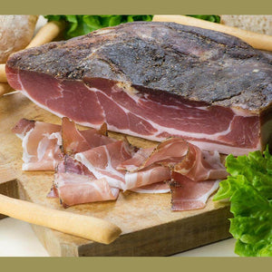 Speck Artigianale Calabrese displayed on a cutting board with slices and fresh greens.
